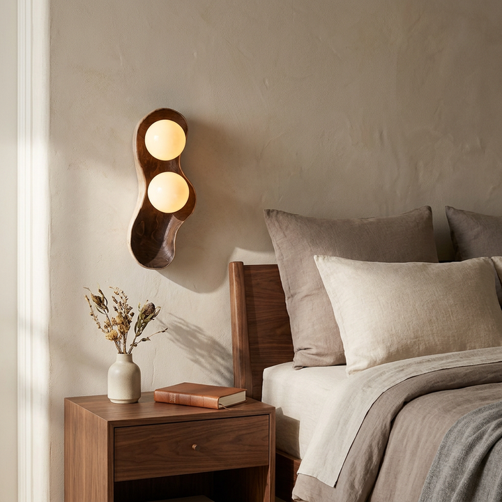 NYRVEQO Dualis Rootlight Wall Lamp with organic carved wood form and two glass globes, shown beside a bed